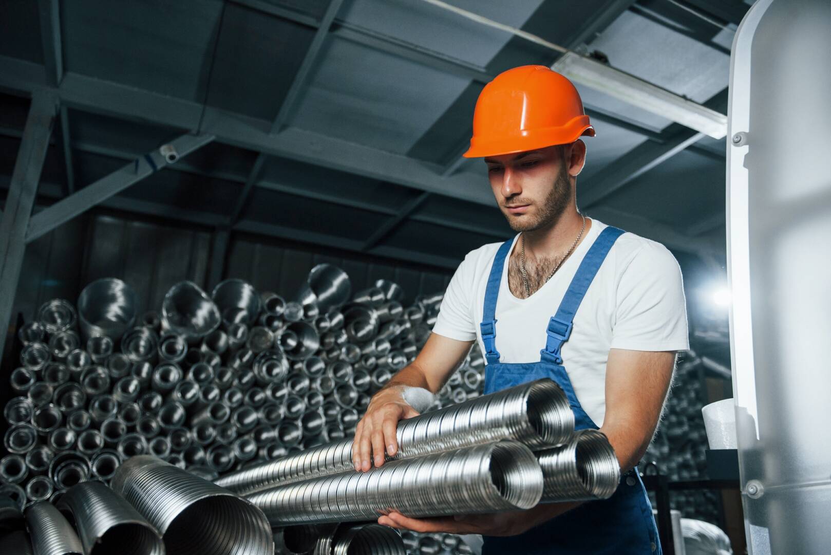 Takes ventilation pipes. Man in uniform works on the production. Industrial modern technology